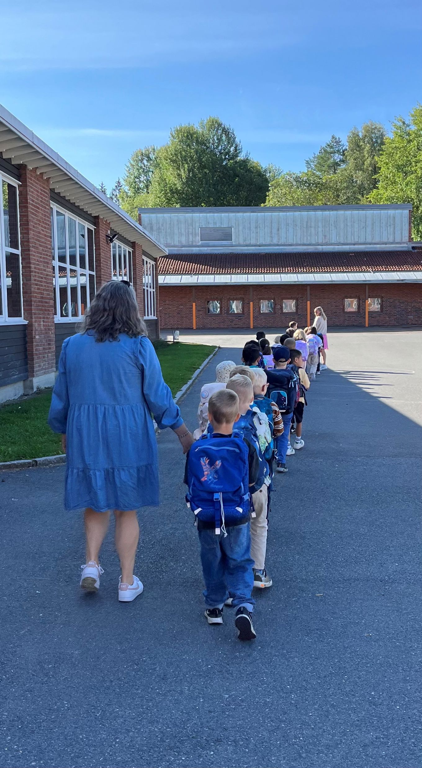 Elever i en førsteklasse som går på rekke og rad gjennom skolegården.